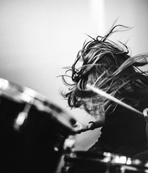 A 9 year old girl has fun playing a drum set in her room, working on songs for her band.  High contrast black and white image.
