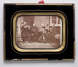 Porträtt_av_stråkkvartett._Fyra_män_sittande_utanför_litet_hus._Säter._Trol._1860-tal_-_Nordiska_Museet_-_NMA.0052718_1